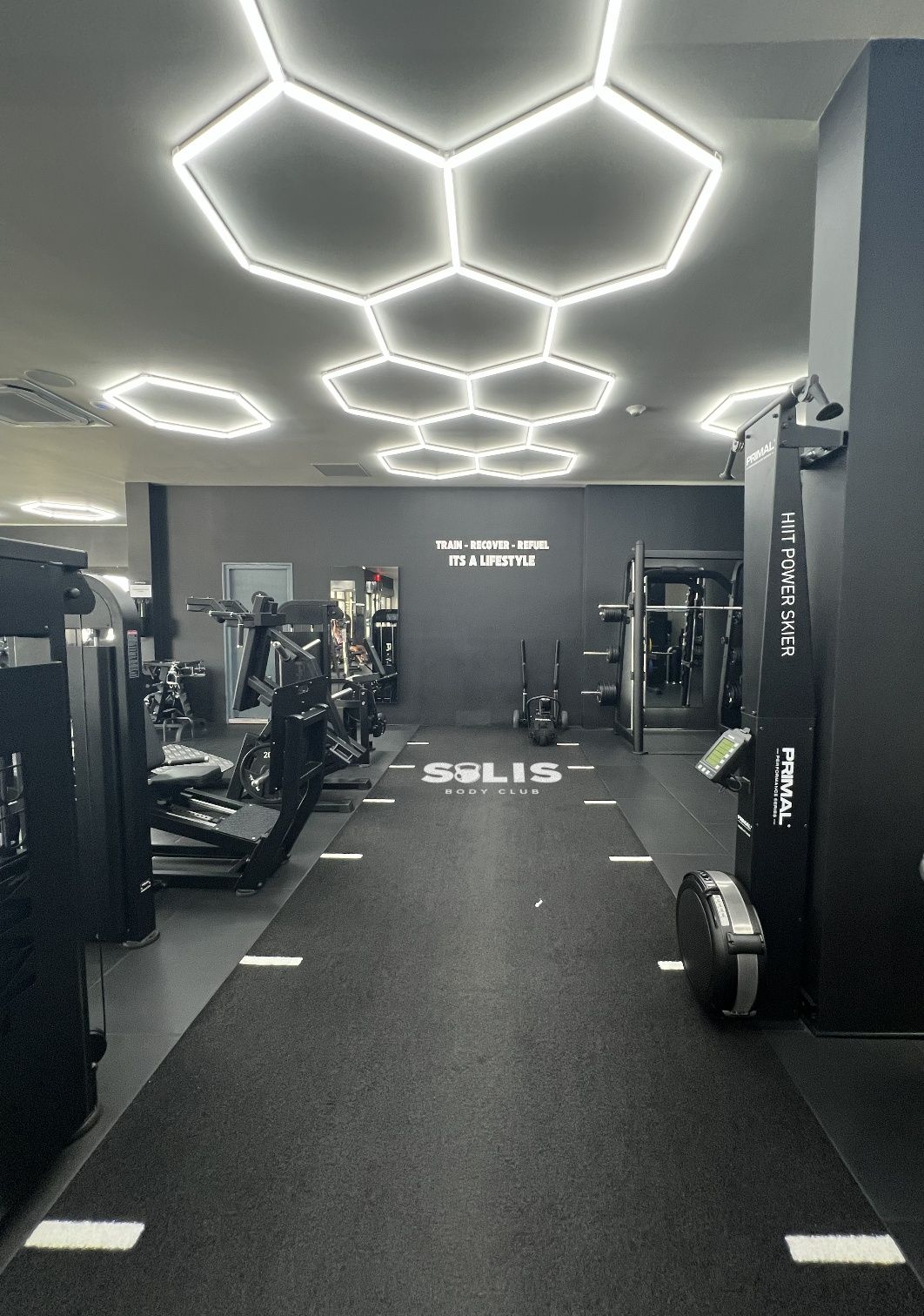 The Solis logo on the turf, a Primal HIIT Power Skier and the Train – Recover – Refuel wall