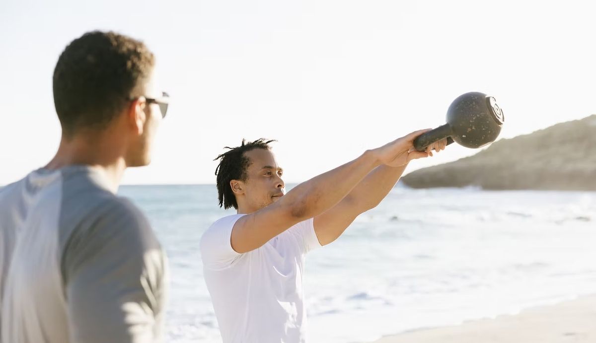 Brendan Webster coaching a client through a kettlebell swing on the beach in St. Maarten