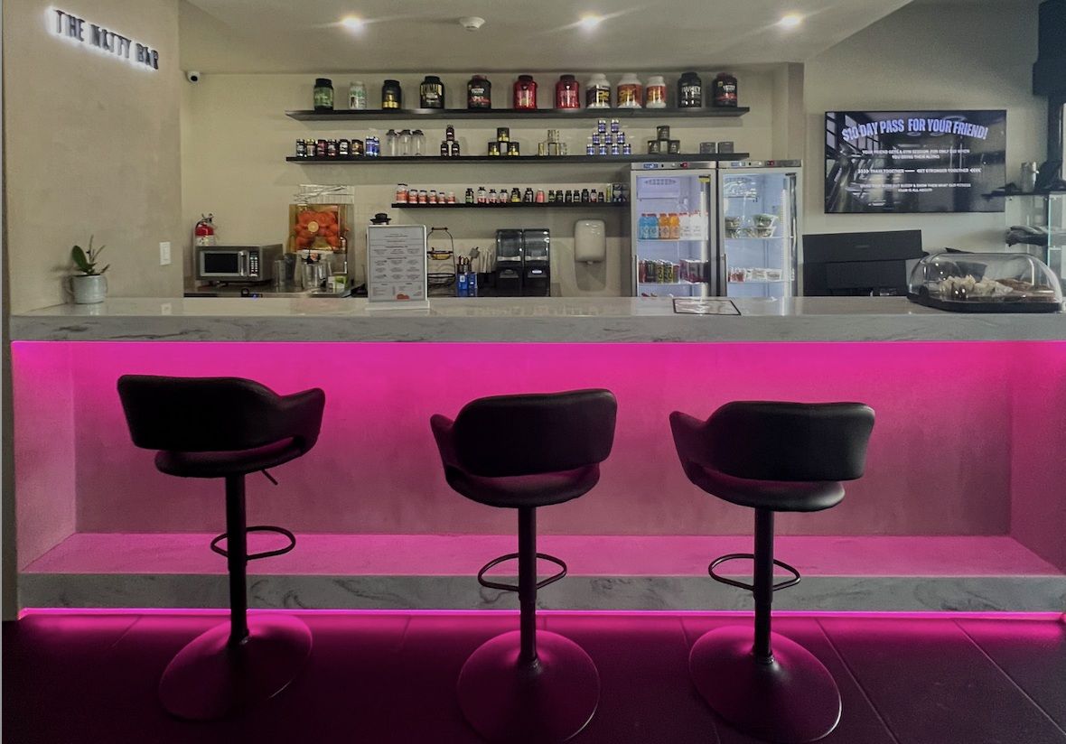 The smoothie bar at Solis Body Club: pink-lit counter, three bar stools, protein shelves and drinks fridges
